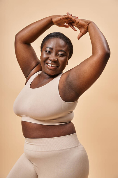 улыбка плюс размер женщина в бежевом белье позирует с поднятыми руками, тело положительное и самоуважение - Фото, изображение