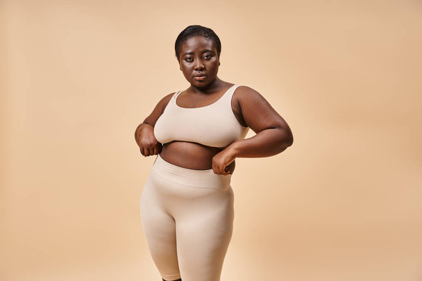 mujer de talla grande en ropa interior posando sobre fondo beige, potenciación corporal positiva y femenina - Foto, imagen
