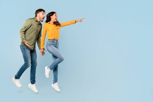 Joyful man and woman enthusiastically pointing to something off-camera at free space, expressing surprise and delight on a light blue background, banner - Photo, Image
