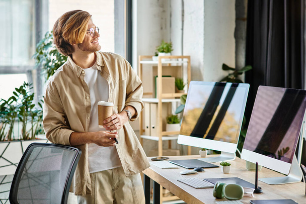 весёлый человек в очках держит кофе и перо стилуса в современной офисной обстановке, постпродакшн - Фото, изображение