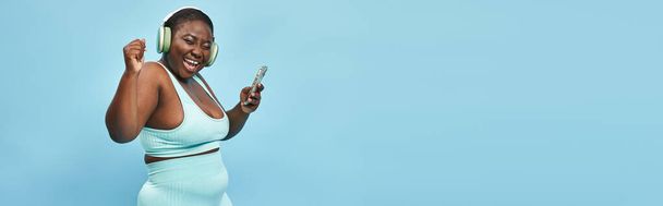 συν μέγεθος αφρικανή αμερικανίδα γυναίκα ακούγοντας μουσική σε ακουστικά συνδεδεμένα με smartphone, banner - Φωτογραφία, εικόνα