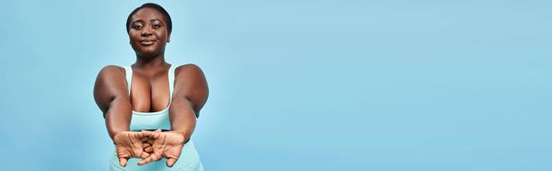 heureuse femme afro-américaine taille plus en tenue active s'étirant joyeusement sur fond bleu, bannière - Photo, image