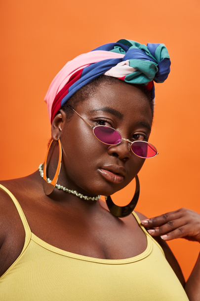 retrato de jovem mulher americana africana plus size em lenço de cabeça e óculos de sol na moda em laranja - Foto, Imagem