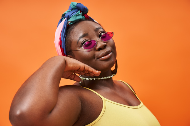 Fashionable and plus size african american woman in headscarf and trendy sunglasses on orange - Photo, Image