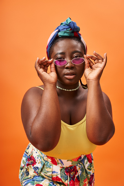 Модний плюс розмір афроамериканської жінки в окулярах в модних сонцезахисних окулярах на помаранчевому - Фото, зображення