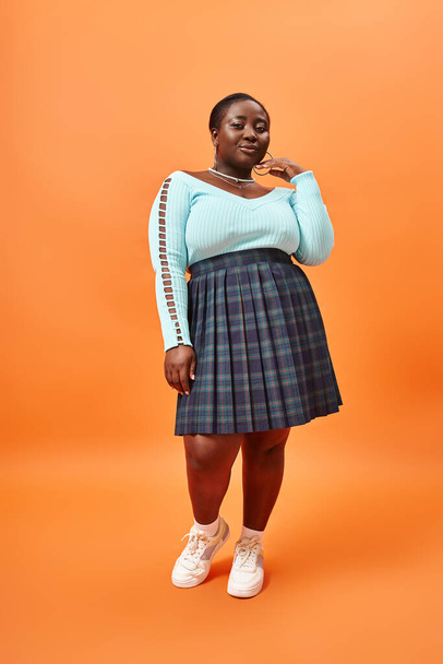 plus size african american model in plaid skirt and mint color jumper posing on orange backdrop - 写真・画像