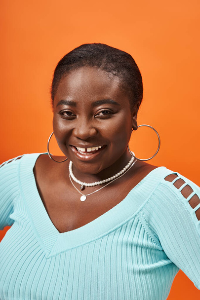 positive plus size african american woman in blue long sleeve posing on orange background - Photo, Image