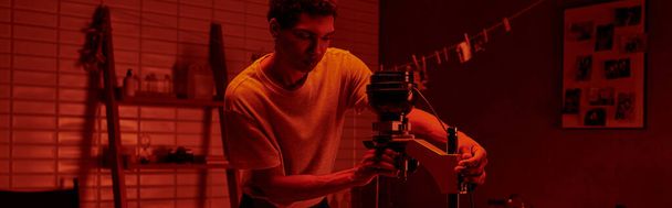 カメラマンは,赤いライト,バナーで暗室でフィルムを拡大する繊細なプロセスに焦点を当てています - 写真・画像