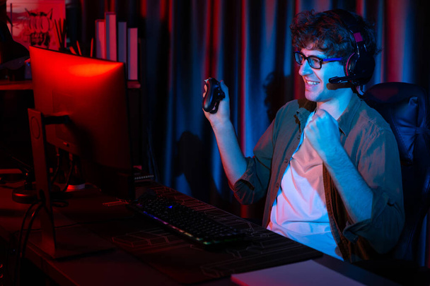 Uśmiechnięty młody strumień gier zwycięski zespół grający z joystick na Esport online na komputerze walki gry dla konkurentów na planowaniu strategii na następny trudniejsze w czerwonym neon oświetlenia nowoczesny pokój. Pędziwiatr. - Zdjęcie, obraz