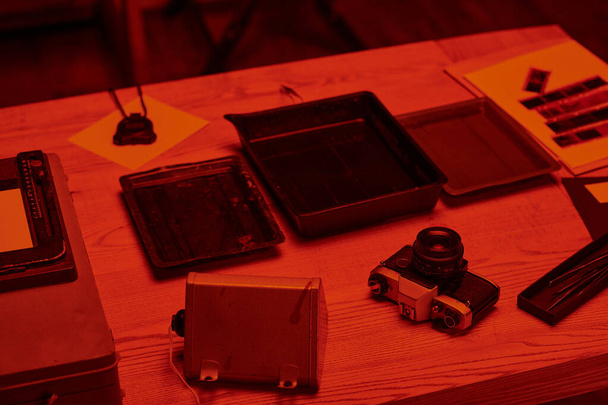Analog kamera ve film geliştirme araçlarıyla dolu bir masa. Karanlık odada kırmızı ışık ve nostalji ile. - Fotoğraf, Görsel