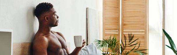 Düşünceli, üstsüz, kahve fincanı olan Afro-Amerikan bir adam yatak odasında oturuyor ve başını çeviriyor. - Fotoğraf, Görsel
