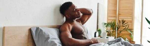jonge Afro-Amerikaanse man met gesloten ogen en gespierde romp zittend en zich uitstrekkend op bed, spandoek - Foto, afbeelding