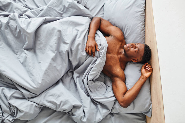 朝の自宅で快適なベッドで寝ているハンサムな運動アフリカ系アメリカ人男性のトップビュー - 写真・画像