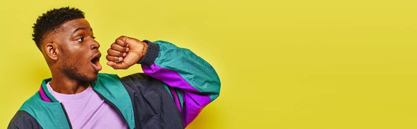 イエロー,バナーを見下ろすスタイリッシュなウインドブレーカーのジャケットで驚いたトレンディなアフリカ系アメリカ人男性 - 写真・画像