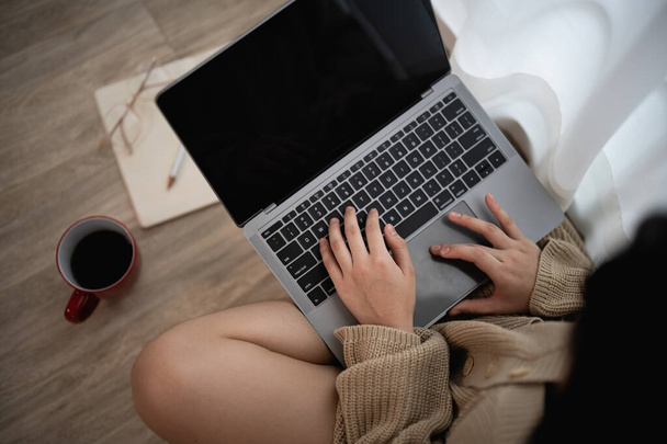 Nahaufnahme einer Frau, die am Laptop arbeitet und auf dem Boden sitzt und Kaffee mit einer Tasse Kaffee trinkt. Selbstständiges Geschäftskonzept. - Foto, Bild