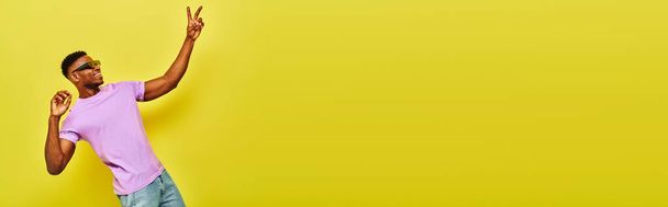 onnellinen musta mies trendikäs kesä asu ja aurinkolasit osoittavat voiton merkki keltainen, banneri - Valokuva, kuva