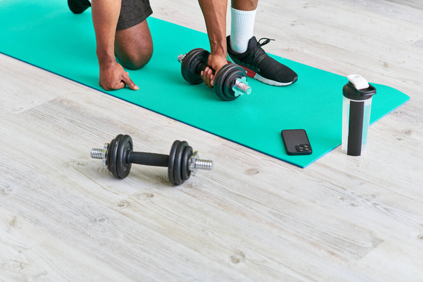 cropped view of african american man training with dumbbell near smartphone and sports bottle - Photo, Image