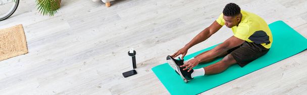 young african american man in stylish sportswear stretching on fitness mat in living room, banner - Photo, Image