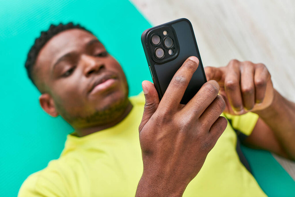 vysoký úhel pohledu na atletický africký Američan muž ve sportovním oblečení procházení internetu na smartphone - Fotografie, Obrázek