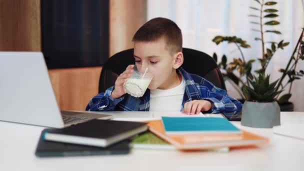 Schlaues Kind mit Milchglas und Schreibtisch für Schreibtisch mit bunten Arbeitsbüchern während des Online-Unterrichts. Die Bedeutung gesunder und nahrhafter Snacks für eine erfolgreiche Bildung von Kindern. - Filmmaterial, Video