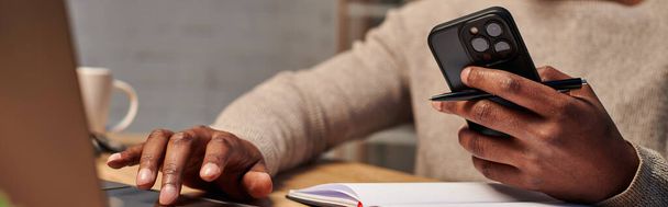 vista ritagliata dell'uomo afroamericano con smartphone mentre lavora a casa, banner - Foto, immagini