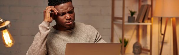 freelancer afro-americano sério trabalhando no laptop no escritório em casa à noite, bandeira horizontal - Foto, Imagem