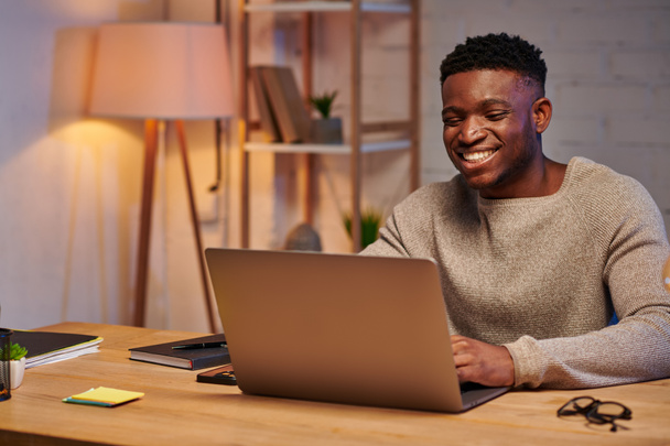fröhlicher afrikanisch-amerikanischer Mann, der nachts im Homeoffice am Laptop arbeitet, selbstständiger Freiberufler - Foto, Bild