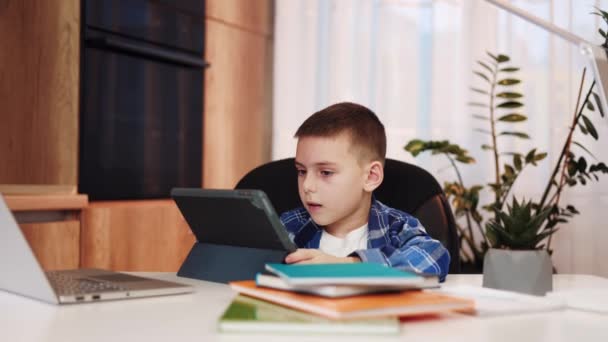 Kleiner Kerl, der sich in der Fernschule durch digitales Tablet engagiert und dabei nützliche Fähigkeiten und Kenntnisse erlangt. Cleverer Junge recherchiert für sein Schulprojekt, während er zu Hause mit Büchern am Schreibtisch sitzt. - Filmmaterial, Video