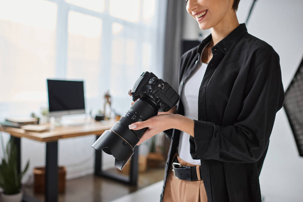 καλλιεργημένη άποψη νεαρής γυναίκας φωτογράφου με casual ρούχα που εργάζεται στο στούντιο με διάφορα είδη εξοπλισμού - Φωτογραφία, εικόνα