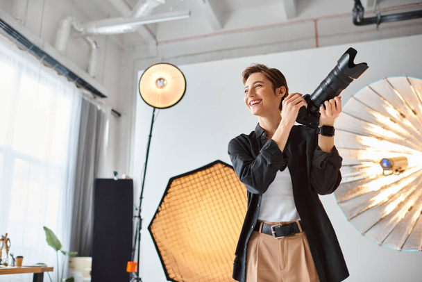 fotógrafa feminina alegre em traje casual com câmera em suas mãos sorrindo e olhando para longe - Foto, Imagem