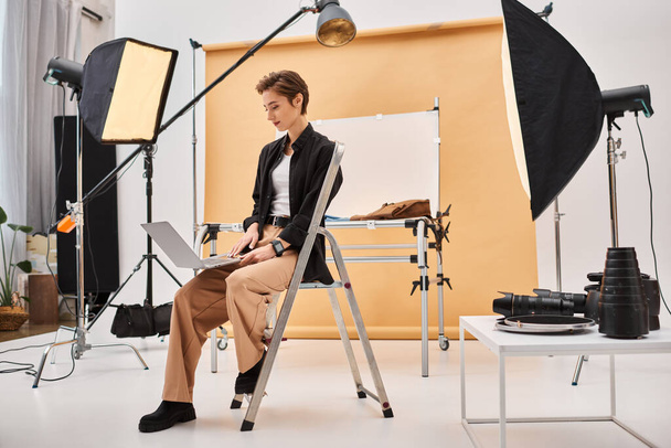 gyönyörű rövid hajú fotós ül és retusálás fotók a stúdióban segítségével a laptop - Fotó, kép