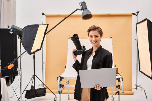 fröhliche attraktive Frau, die glücklich lächelt, während sie Fotos retuschiert und ihre Kamera im Studio hält - Foto, Bild