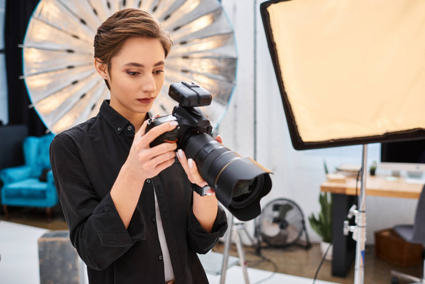 ελκυστική συμπυκνωμένη γυναίκα σε casual ενδυμασία τραβώντας φωτογραφίες με τη σύγχρονη φωτογραφική μηχανή της στο στούντιο της - Φωτογραφία, εικόνα
