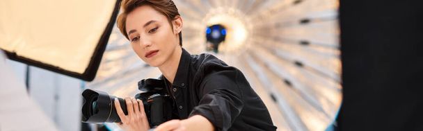 atraktivní zaměřená fotografka držící fotoaparát a připravující se na focení ve svém studiu - Fotografie, Obrázek