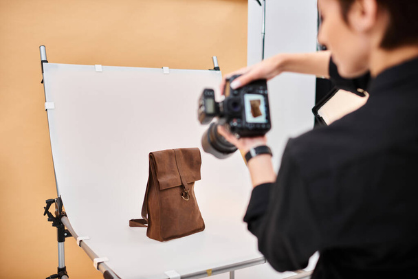 hermosa fotógrafa de pelo corto tomando fotos de mochila de cuero marrón en su estudio - Foto, imagen