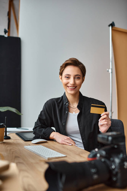 alegre atraente fotógrafo feminino pagando on-line usando seu cartão de crédito e sorrindo para a câmera - Foto, Imagem