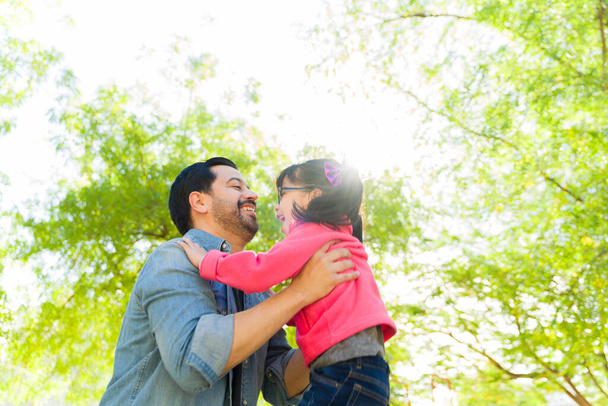 Amare papà sorridente tenendo la sua giovane figlia e giocando un gioco divertendosi insieme all'aperto nel parco - Foto, immagini