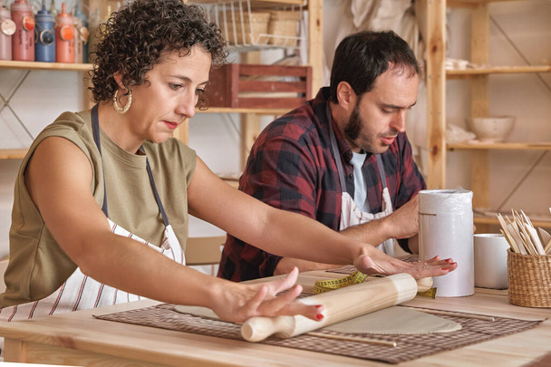 Femme pétrissant l'argile avec rouleau à pâtisserie dans un atelier de céramique. Hobby et concept d'artisanat. - Photo, image