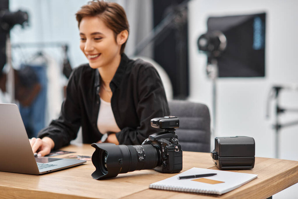 Сосредоточьтесь на современной камере на столе рядом с веселым профессиональным фотографом-женщиной в студии - Фото, изображение