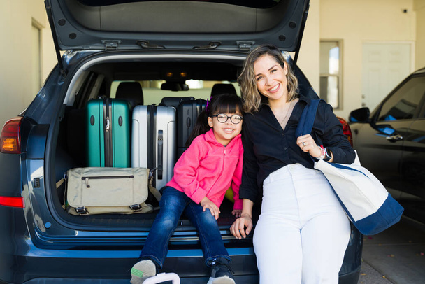 Biała szczęśliwa mama i jej młody dzieciak uśmiechający się nawiązując kontakt wzrokowy podczas wkładania walizek do bagażnika samochodu na wycieczkę - Zdjęcie, obraz