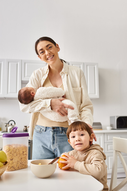cheerful attractive mother enjoying breakfast with her toddler and newborn sons, modern parenting - Photo, Image