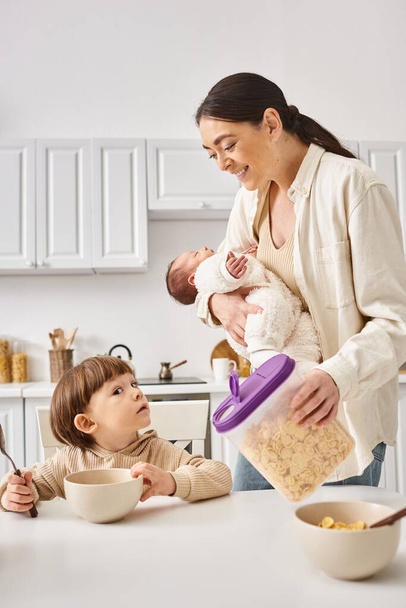 freudige attraktive Mutter beim Frühstück mit ihrem Kleinkind und ihren neugeborenen Söhnen, moderne Elternschaft - Foto, Bild