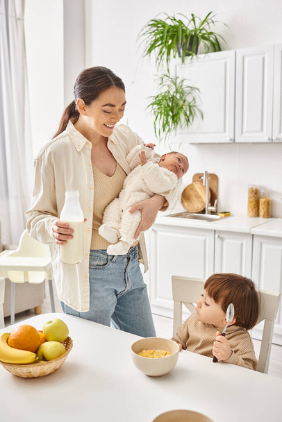 fröhliche schöne Mutter beim Frühstück mit ihrem Kleinkind und ihren neugeborenen Söhnen, moderne Elternschaft - Foto, Bild