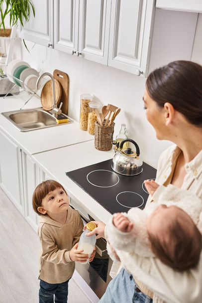 liefdevolle gelukkig moeder in huishouden tijd doorbrengen met haar peuter en pasgeboren zonen tijdens het ontbijt - Foto, afbeelding