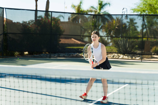 sportief Kaukasisch tiener meisje having plezier buiten het spelen van een tennis spel tijdens haar lessen  - Foto, afbeelding