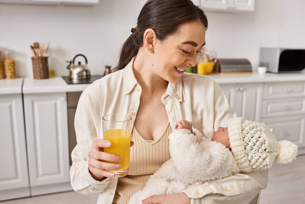 happy beautiful woman in homewear holding her cute baby boy and glass of orange juice, parenting - Photo, Image