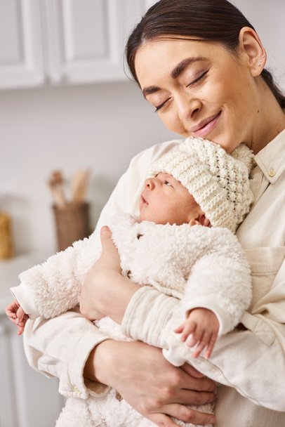 schöne fröhliche Frau in gemütlicher Hauskleidung posiert mit ihrem netten neugeborenen Jungen, moderne Elternschaft - Foto, Bild