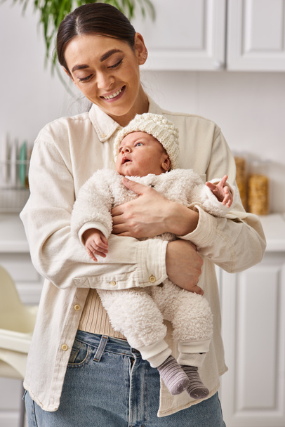 attraktive lustige Frau in bequemer Homewear posiert mit ihrem netten neugeborenen Jungen, moderne Elternschaft - Foto, Bild