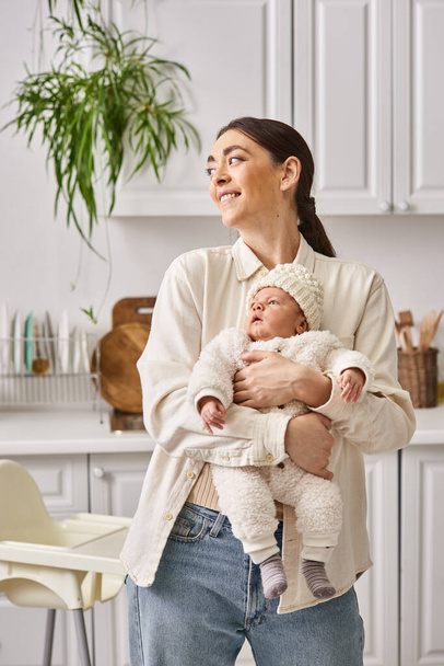 aantrekkelijke vrolijke vrouw in comfortabele homewear poseren met haar schattige pasgeboren baby jongen, moderne ouderschap - Foto, afbeelding