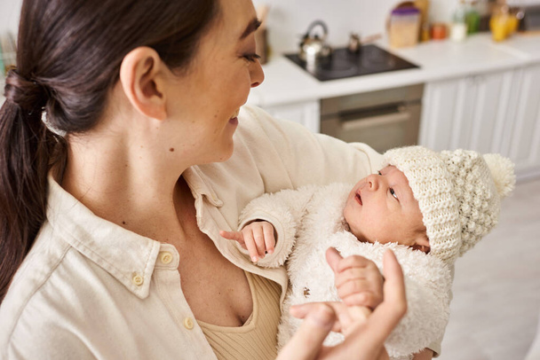Güzel ve sevgi dolu bir anne rahat bir ev elbisesi içinde bebeğine sımsıkı sarılıyor, modern ebeveynlik. - Fotoğraf, Görsel